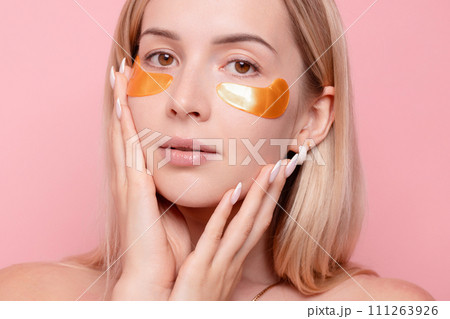Portrait of pretty girl applying golden collagen patches under her eyes in unusual way. Woman facial treatment . Cosmetology, beauty and skincare around eyes, preventing wrinkles. Portrait of pretty girl applying golden collagen patches under her eyes in unusual way. Woman facial treatment . Cosmetology, beauty and skincare around eyes, preventing wrinkles. 111263926
