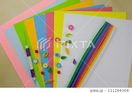 Quilling technique. Rolled colored paper for decoration on a table with paper strips. Develop fine motor skills with paper and a special hobby tool Quilling technique. Rolled colored paper for decoration on a table with paper strips. Develop fine motor skills with paper and a special hobby tool 111264309