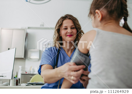 Doctor examining young girl, measuring blood pressure, using medical blood pressure monitor. Concept of preventive health care for children. Doctor examining young girl, measuring blood pressure, using medical blood pressure monitor. Concept of preventive health care for children. 111264929