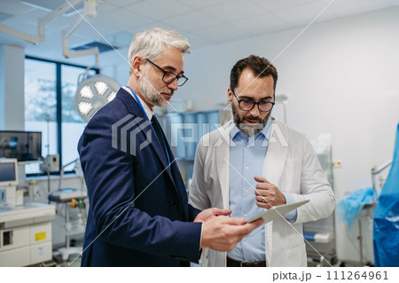 Pharmaceutical sales representative presenting new medication to doctor in medical building, holding box with medication samples. 111264961