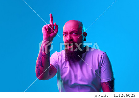 Emotive shocked beard bald man raising finger up, expressing ideas against blue background in neon light 111266025