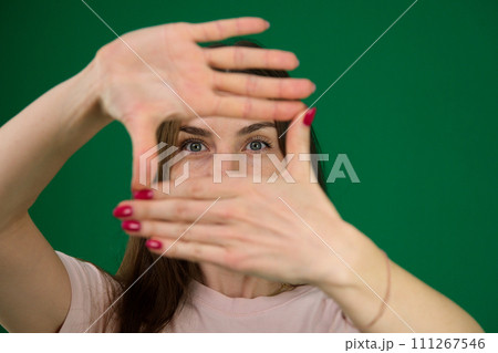 beautiful girl framing her face with her hands different emotions of a young girl on a green background chromakey beautiful facial features real people pink T-shirt white skinned. European 111267546