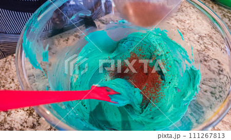 In a well-lit kitchen, an assortment of buttercream frosting in various shades of green and other colors is being meticulously mixed and prepared for the artistic decoration of cupcakes in charming 111267813