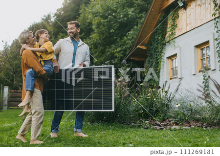 Father mother and daughter standing in garden with solar panel. Solar energy and sustainable lifestyle of young family. Concept of green energy and sustainable future for next generations. Father mother and daughter standing in garden with solar panel. Solar energy and sustainable lifestyle of young family. Concept of green energy and sustainable future for next generations. 111269181