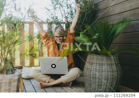 Woman working in the garden, with laptop on legs, celebrating success. Businesswoman working remotely from outdoor homeoffice. Concept of outdoor home office. Woman working in the garden, with laptop on legs, celebrating success. Businesswoman working remotely from outdoor homeoffice. Concept of outdoor home office. 111269204