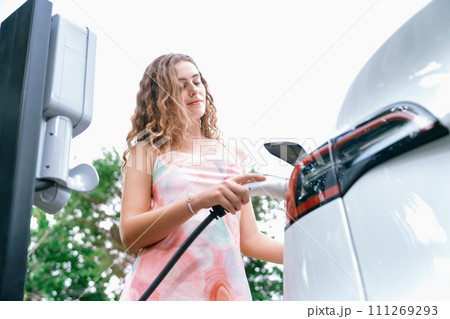 Eco-friendly conscious woman recharging modern electric vehicle. Synchronos 111269293