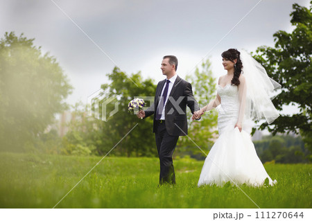 The bride and groom walk on the green grass in the park 111270644