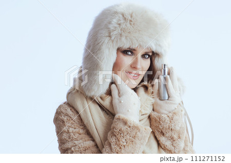 smiling woman in winter coat and fur hat touching face on white 111271152