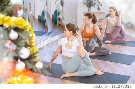 Girl teacher conduct yoga lesson for girls and doing Lord of fishes pose in New Year atmosphere. Girl teacher conduct yoga lesson for girls and doing Lord of fishes pose in New Year atmosphere. 111272356