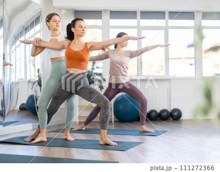 Happy woman standing yoga pose and making full body stretching workout by female trainer in sports room 111272366
