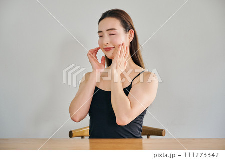 顔をマッサージして肌のお手入れをする30代女性 111273342