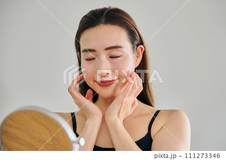 顔をマッサージして肌のお手入れをする30代女性 111273346
