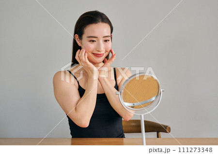 顔をマッサージして肌のお手入れをする30代女性 111273348
