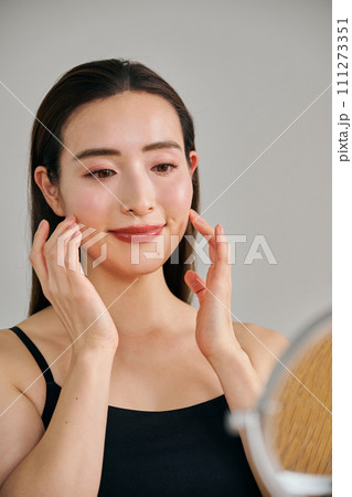 顔をマッサージして肌のお手入れをする30代女性 111273351