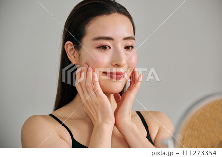 顔をマッサージして肌のお手入れをする30代女性 111273354