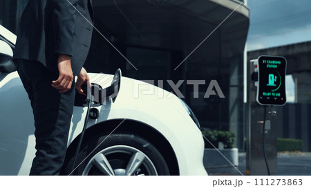 Businessman recharge his electric car from charging station. Peruse Businessman recharge his electric car from charging station. Peruse 111273863
