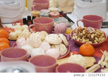 marshmallow tea cups delicious snack nuts dried fruits and tangerines on the table sweets good presentation healthy self-care treats for guests on a wicker woolen tablecloth napkin 111274132