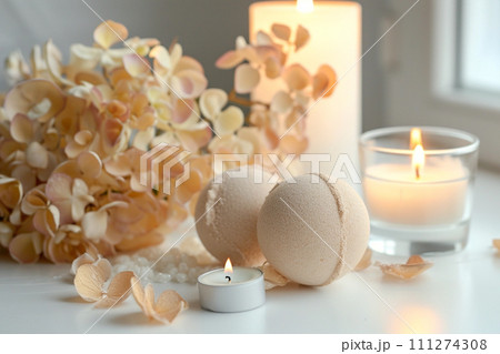 Beige golden bath bombs with hortensia on white table, lit candle Beige golden bath bombs with hortensia on white table, lit candle 111274308