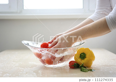 female hands close-up wash cherry tomatoes in clean spring water in a glass bowl yellow pepper cilantro leaves nearby cleanliness healthy tasty food salad vegetables diet healthy food vitamins 111274335
