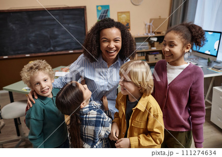 Portrait of happy female teacher with diverse group of little children enjoying class together in school 111274634