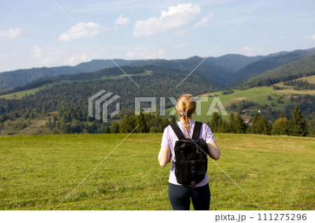 30s Girl with backpack on mountain peak with green grass looking at beautiful mountain valley in fog at sunset in summer. Landscape with sporty young woman, rear view 30s Girl with backpack on mountain peak with green grass looking at beautiful mountain valley in fog at sunset in summer. Landscape with sporty young woman, rear view 111275296