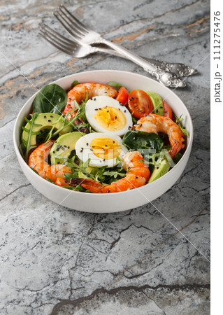 Mediterranean shrimp salad with avocado, arugula, spinach, tomatoes and boiled eggs close-up in a bowl. Vertical Mediterranean shrimp salad with avocado, arugula, spinach, tomatoes and boiled eggs close-up in a bowl. Vertical 111275476