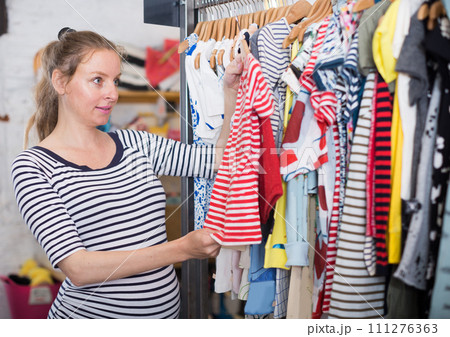Pregnant woman in striped tunic chooses shirt in clothing shop 111276363
