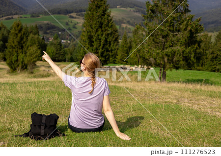 Back view of Woman in active trekking clothes having a halt after hiking. Travel and active lifestyle concept. 30s girl enjoying valley view from top of a mountain, outdoor activities 111276523