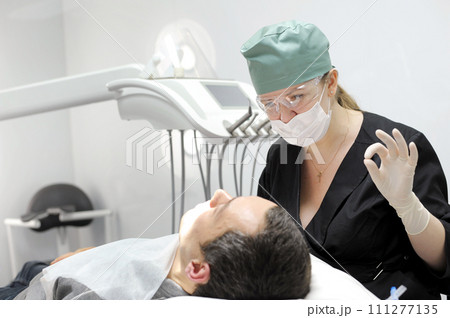 female doctor dentistry showing fingers OK operation she will do on her mask goggles Green cap and black clothes dentistry latest technology white background dental treatment examination 111277135