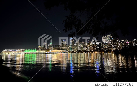 Mirror reflection of the whole city in the ocean Dark night in Canada Vancouver view from ocean luminous building Canada Place sails in green Skyscrapers glow with many lights reflected in the water 111277269