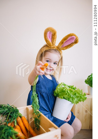 Cute little child girl wearing bunny ears on Easter day and holding carrot in hand 111280994
