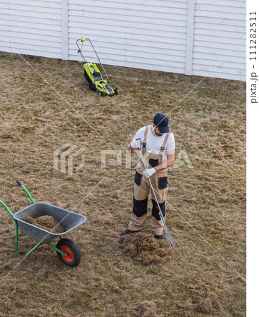 Scarifying lawn with rake and scarifier, Man gardener scarifies the lawn and removal of old grass 111282511