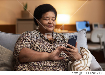Portrait of plump Black senior woman using smartphone in cozy home and tapping touchscreen copy space Portrait of plump Black senior woman using smartphone in cozy home and tapping touchscreen copy space 111284212