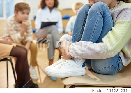 Close up of depressed young girl hugging knees and sharing mental health problem during support group for childrenwith copy space 111284231