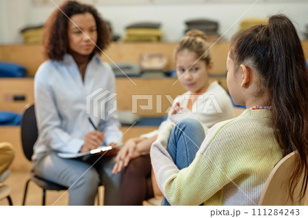 Back view of unrecognizable teen girl sharing mental health problems during support group meeting for childrenwith copy space Back view of unrecognizable teen girl sharing mental health problems during support group meeting for childrenwith copy space 111284243