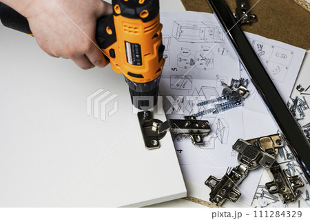 Installing a furniture hinge on the door. Assembling furniture and fixing fittings close-up. Screwing the door hinge onto a piece of furniture with a screwdriver. 111284329