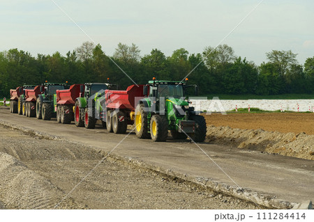 A group of tractor-dump trucks standing on a road section being repaired. 111284414