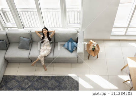 Relaxed young Asian woman resting on large comfortable sofa Relaxed young Asian woman resting on large comfortable sofa 111284502