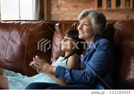 Happy preteen latina girl relax on couch in grandmother embraces 111285035