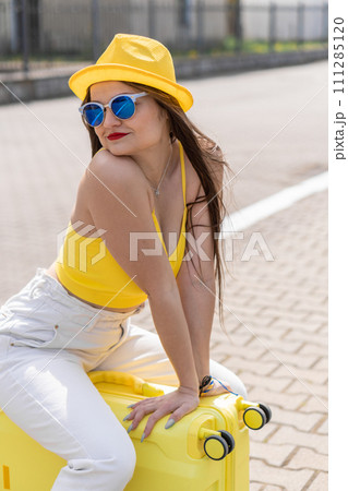 Conquest of new horizons: a stylish traveler in a yellow look feels excitement before the price. To new adventures: a girl in a stylish yellow look happily sits on a suitcase, ready to leave. 111285120