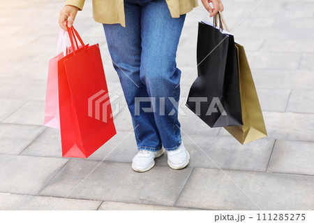 Cropped portrait of unrecognisable woman with colourful shopping bags on urban shopping mall background. Purchases, black friday, discounts, sale concept. Online shopping concept, Seasonal Sales. 111285275