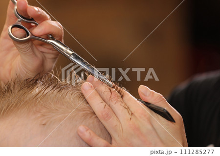Men's hairstyling, haircutting, in a barber shop or hair salon. Close-up of man hands grooming kid boy hair in barber shop. Portrait of male child at the barber shop to cut his hair. 111285277