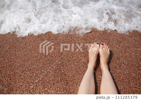 Travel concept - Woman's legs on beautiful tropical beach with pebble sand. Feet on sand and wave in summer time. girl barefoot in ocean water on vacation travel. Feel happy and relax. copy space. 111285379