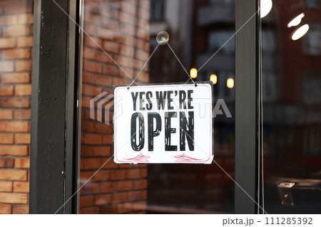 Inscription Yes we're open metal plate with black and white sign on glass door store, cafe, beautystore, barbershop after coronavirus lockdown quarantine. business reopen again 111285392