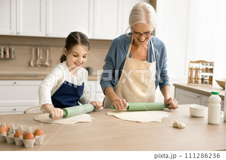 Sweet grandkid helping positive attractive grandma in apron to bake 111286236