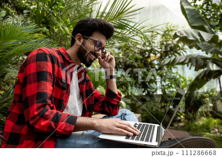 Man in red checkered shirt working on laptop in a garden Man in red checkered shirt working on laptop in a garden 111286668