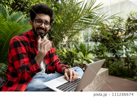 Hindu man in checkered shirt working on laptop in the garden 111286674