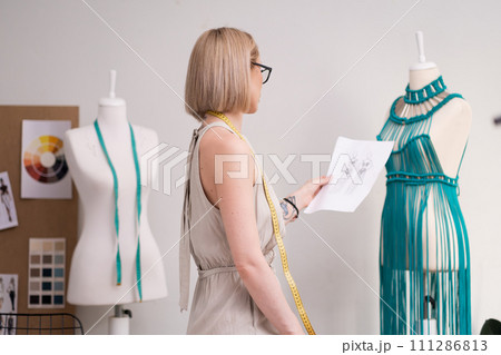 Dressmaker learns dress sketch near mannequin with craft macrame dress in sewing atelier creative designer sews elegant women garment in dressmaking workshop 111286813