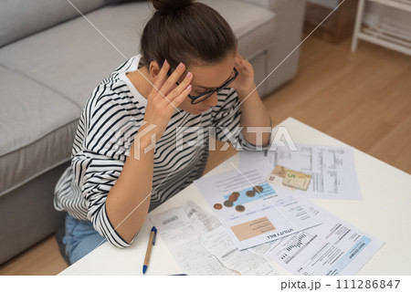 Debt-Stricken Distress: An unhappy woman, burdened by debt, grapples with managing household finances, calculating expenses, and making online payments. Debt-Stricken Distress: An unhappy woman, burdened by debt, grapples with managing household finances, calculating expenses, and making online payments. 111286847