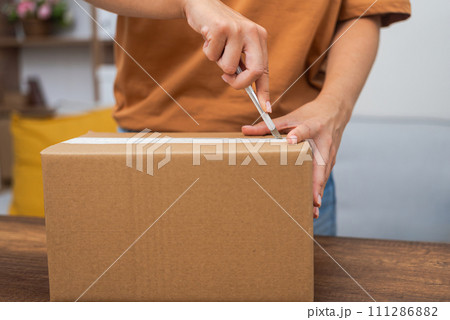 A young lady use utility knife to open package mock up , unboxing the cardboard box online shopping.  111286882